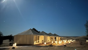 Un grand bâtiment moderne, conçu comme une tente et comprenant plusieurs pièces, situé dans un environnement désertique.