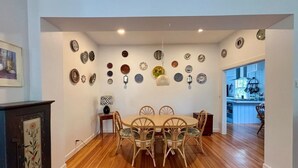 A dining area with a wooden floor, a round table with chairs, and a wall decorated with various plates. - Original School House in the Heart of Chatham (Chatham)