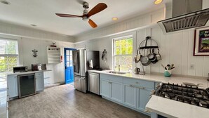 A modern kitchen with white cabinetry, a gas stove, and a ceiling fan. - Original School House in the Heart of Chatham (Chatham)
