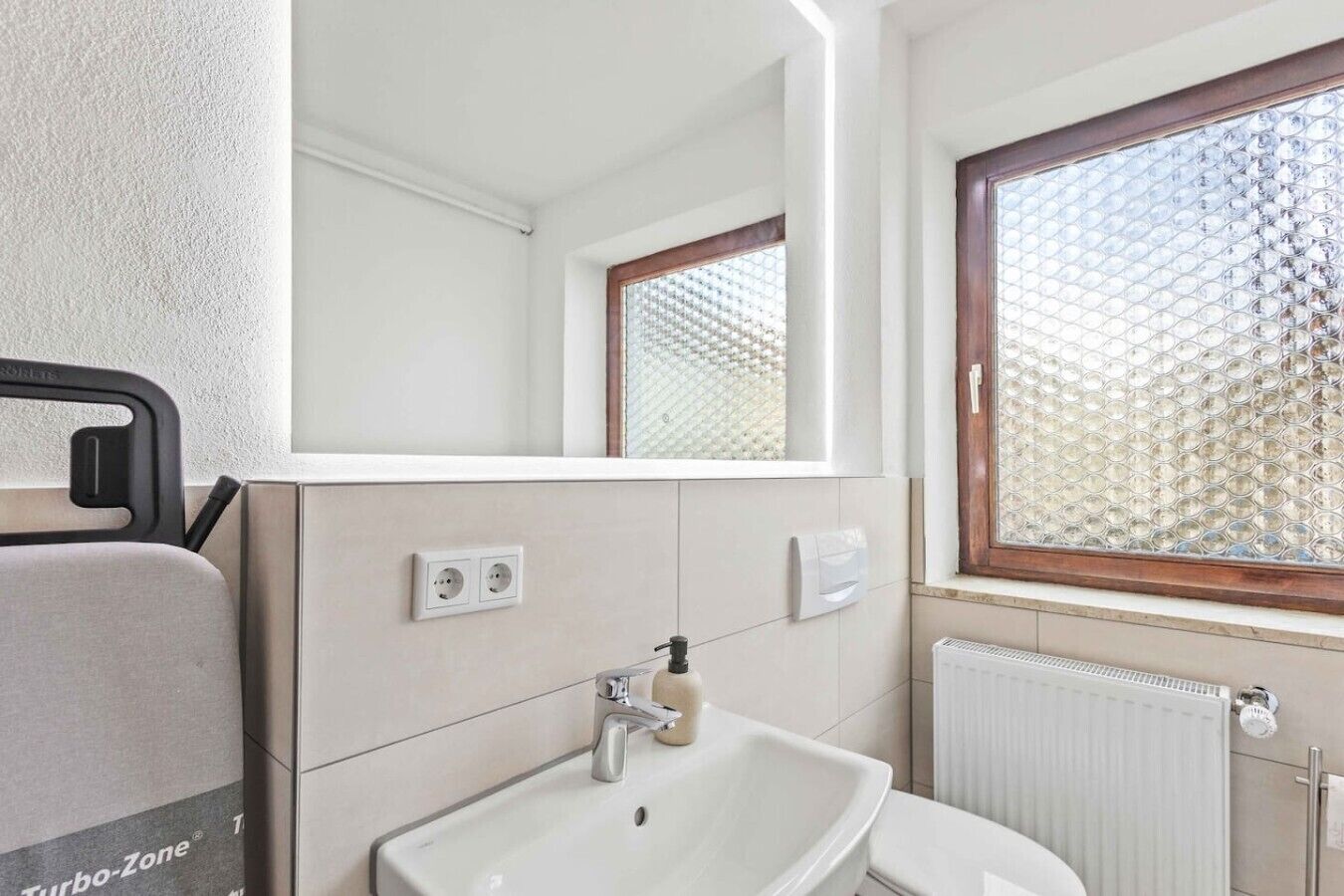 A bathroom with a sink, mirror, window, and radiator.