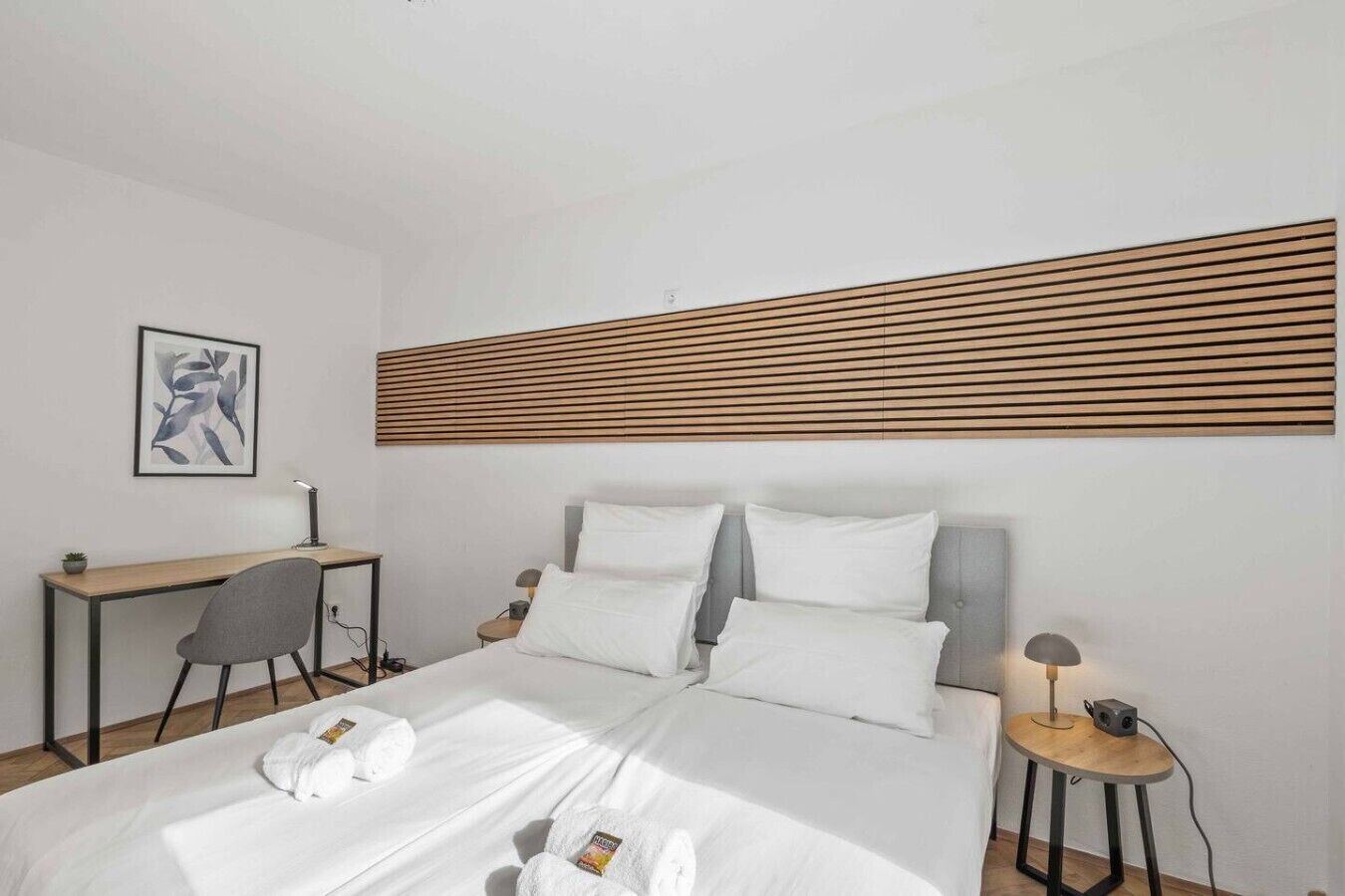 Une chambre d’hôtel comprenant un lit, des tables de chevet, un bureau, une chaise et un panneau fixé au mur.