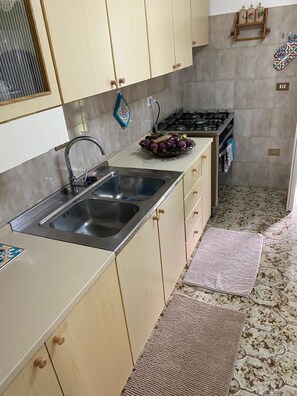 A kitchen with a double sink, wooden cabinets, a gas stove, and a patterned floor. - Villa ferruccio (Scala di Furno)