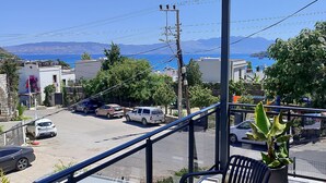 A balcony with a table and chairs, overlooking a street with parked cars and buildings.