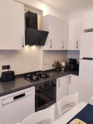 Una cocina moderna con armarios blancos, una campana extractora Bosch, una estufa a gas Bosch, un lavavajillas Bosch y una cafetera.