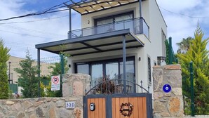 A modern two-story house with a stone wall, a wooden gate, and a balcony.