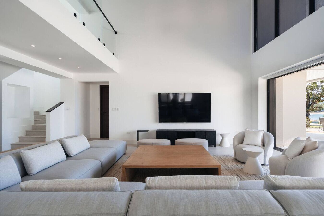 A modern living room with a large flat-screen TV, a sectional sofa, a coffee table, and a staircase leading to an upper level.