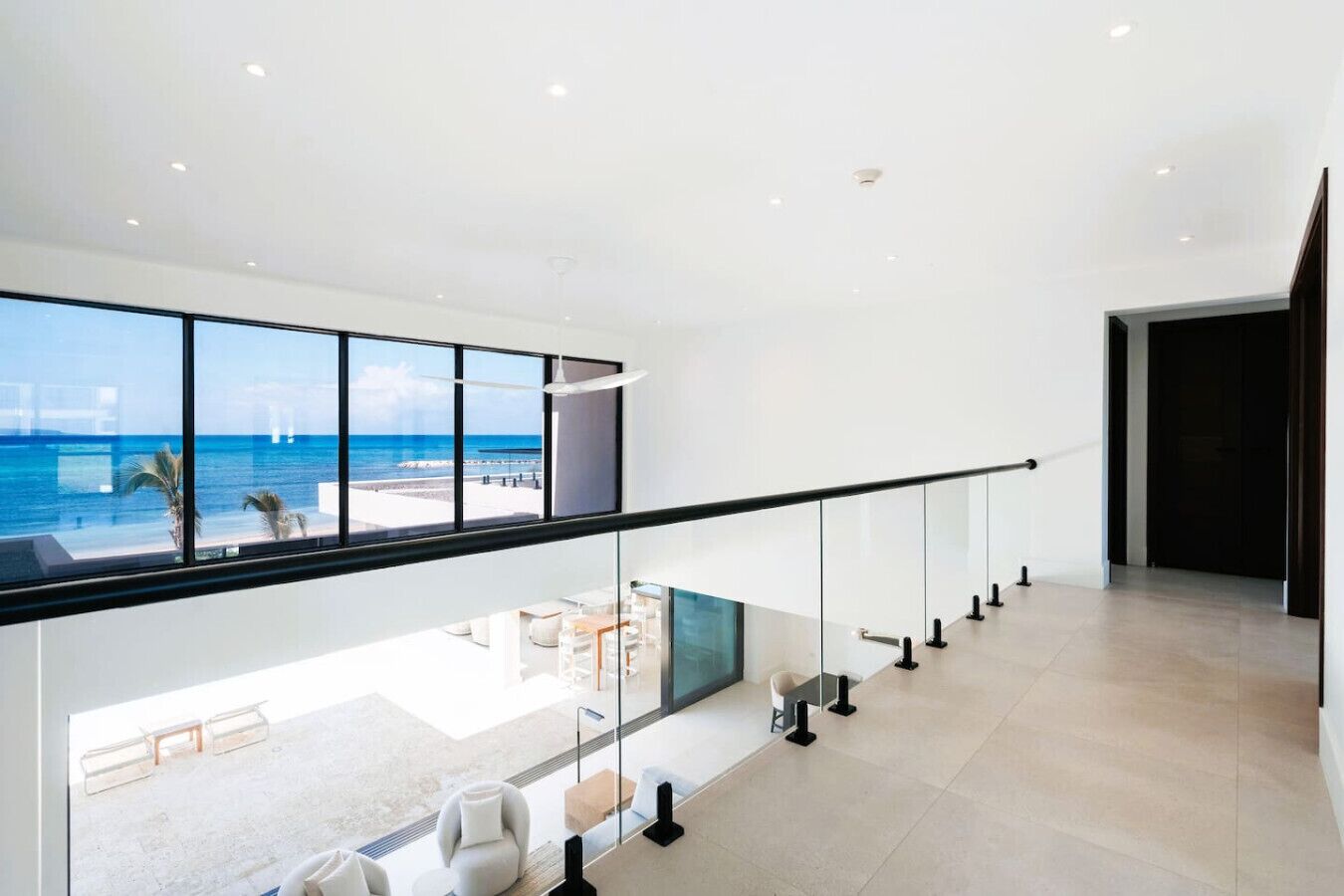 A modern interior with a glass railing overlooking a beach, a spacious seating area, and a view of the ocean.