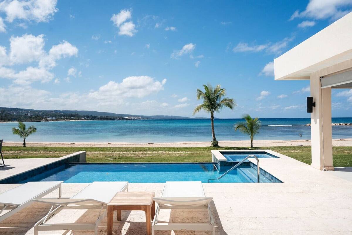 A pool area with lounge chairs, a pool, and a view of the beach and ocean.