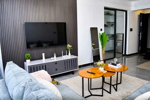 A modern living room with a flat-screen TV, grey sofa, two wooden side tables, and a large mirror. - Stylish 2 Bedroom Apartment in Nairobi with Gym, WiFi, and 24/7 Security (Nairobi)