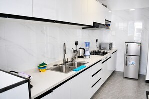A modern kitchen with a stainless steel sink, a gas stove, a microwave, and a refrigerator. - Stylish 2 Bedroom Apartment in Nairobi with Gym, WiFi, and 24/7 Security (Nairobi)