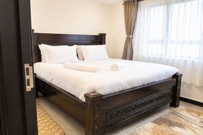 A neatly made bed with white linens in a room with a dark wooden headboard and a patterned rug. - Stylish 2 Bedroom Apartment in Nairobi with Gym, WiFi, and 24/7 Security (Nairobi)