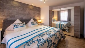 A modern hotel room with a large bed, a mirror, and a stone-textured wall. - Apartment Seehöhe at Maarberg Resort – Holiday Apartment for 4 Guests (48 m²) in Schalkenmehren (Schalkenmehren)