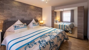 Una habitación de hotel moderna con una cama grande, un espejo y una pared con textura de piedra.