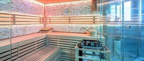 Un sauna avec des bancs en bois, une paroi en verre et un mur en pierre.
