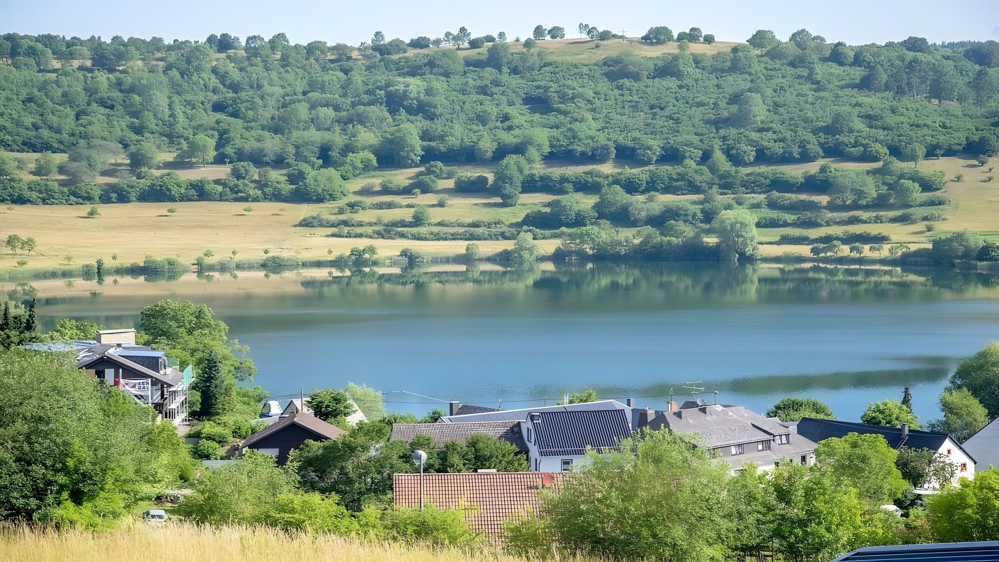 A lakeside view with houses, trees, and a clear sky.