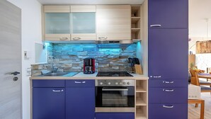 A compact kitchen with a stone backsplash, a coffee maker, and a built-in oven. - Apartment Seehöhe at Maarberg Resort – Holiday Apartment for 4 Guests (48 m²) in Schalkenmehren (Schalkenmehren)