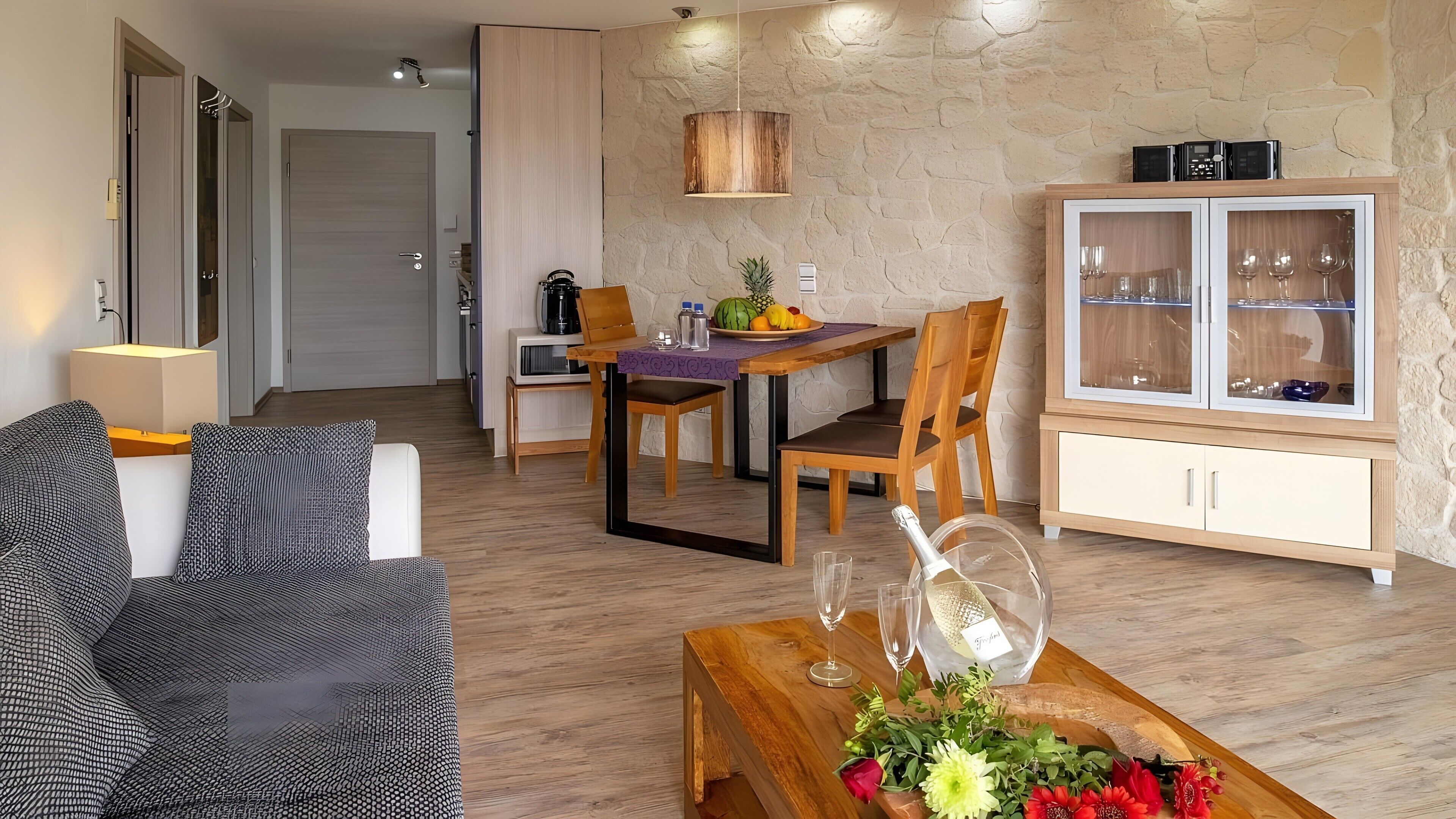 Ein modernes Wohnzimmer mit einer Couch, einem Esstisch mit Stühlen, einer Holzkabine mit Glastüren und einer Steinwand.