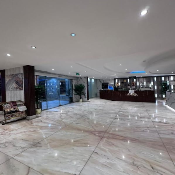 A hotel lobby with a reception desk, marble flooring, and a glass door entrance.