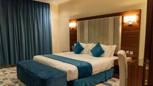 A hotel room with a bed, a desk, a chair, a curtain, and a patterned carpet. - Life Suites Serviced Apartments (Riyadh)