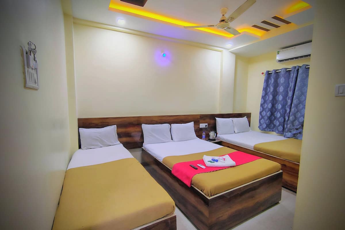 A hotel room with three beds, a ceiling fan, an air conditioner, and a window with curtains.