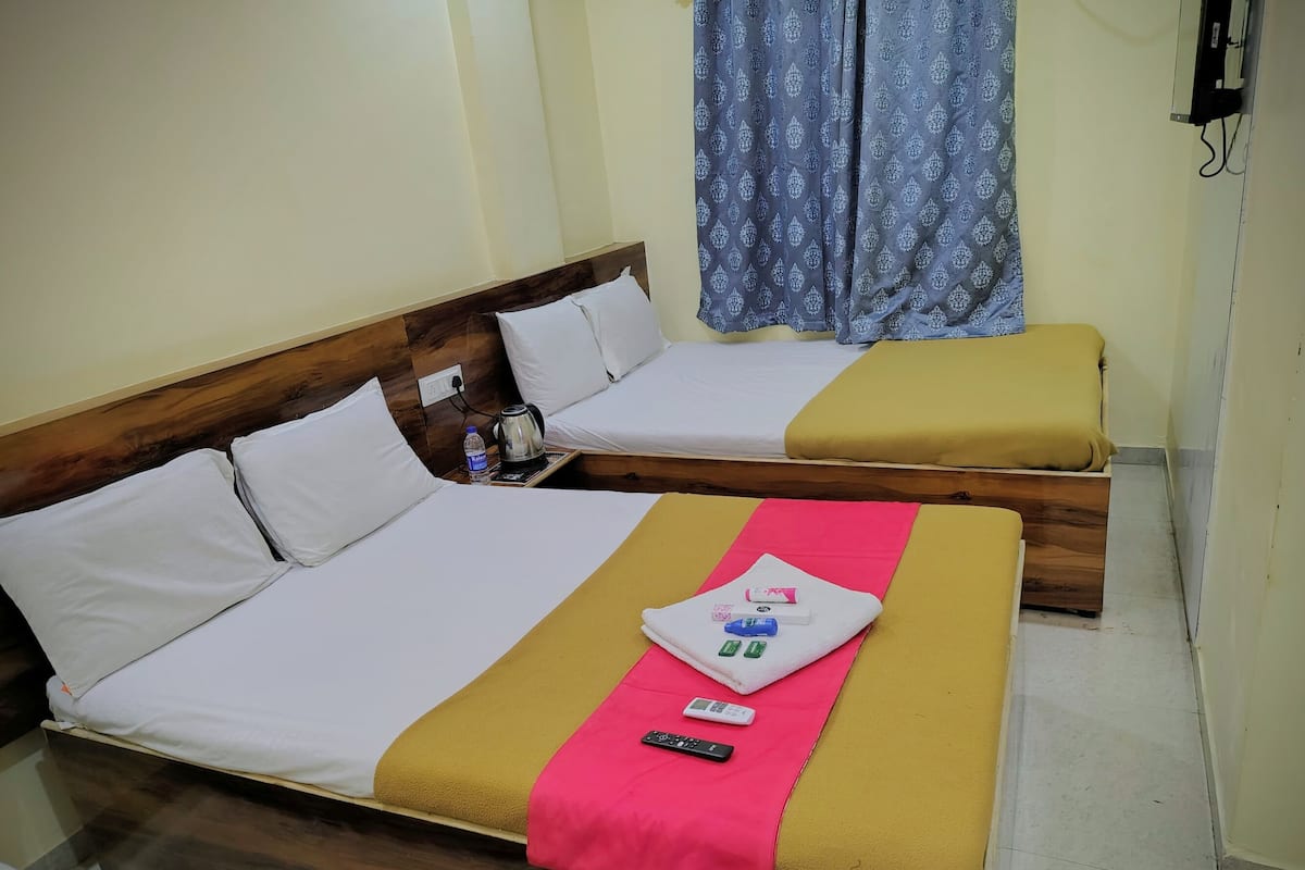 A hotel room with two beds, a wooden headboard, a water bottle, a kettle, a remote control, and a small table.