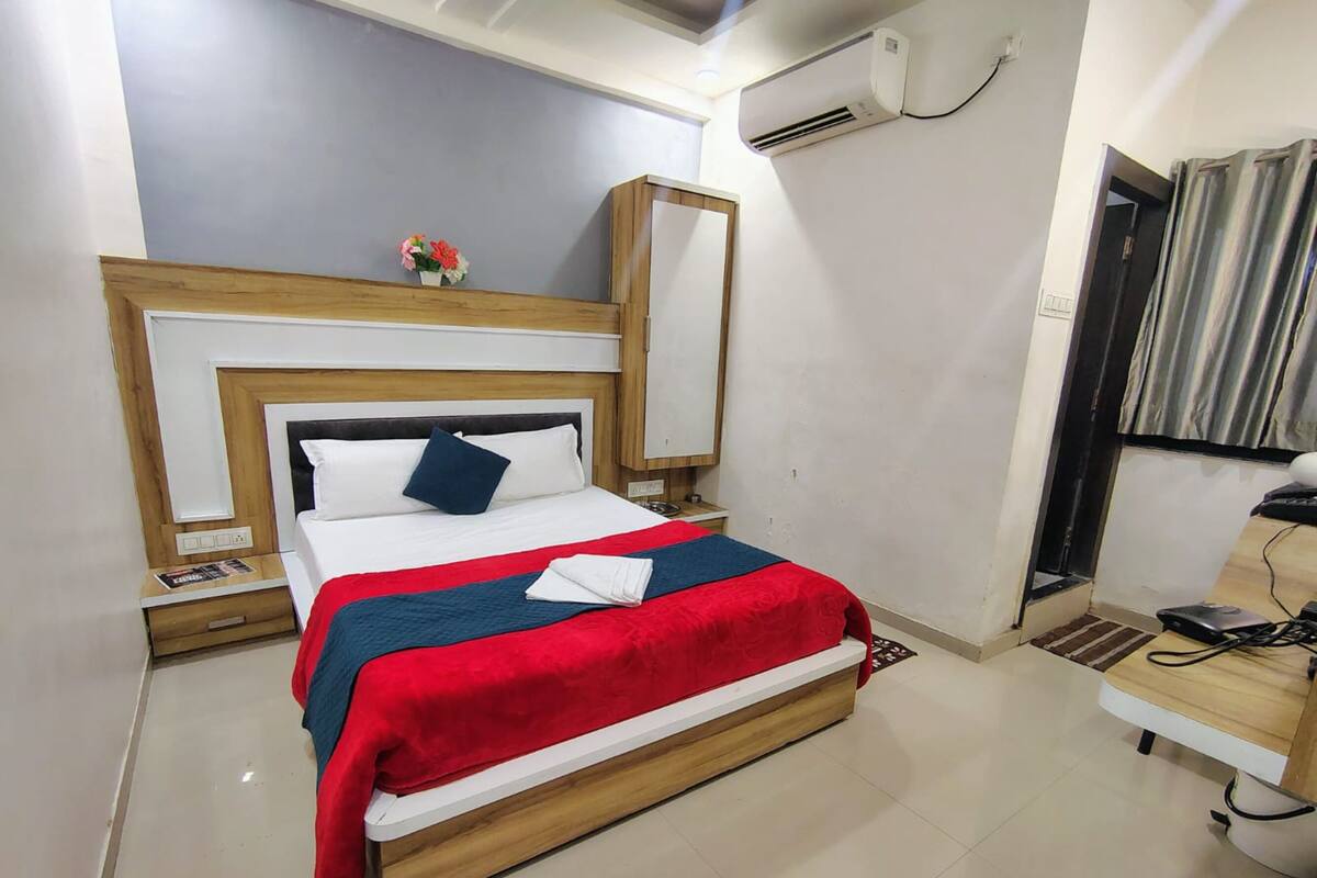 A neatly arranged hotel room with a bed, bedside table, and an air conditioning unit.