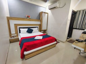 A neatly arranged hotel room with a bed, bedside table, and an air conditioning unit. - Hotel Sai Nanda Shirdi (Shirdi)