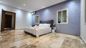 Un dormitorio con cama, mesitas de noche, una lámpara y una ventana.