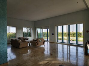 A spacious living room with a large sofa set, a coffee table, and a view through large sliding glass doors to a garden.
