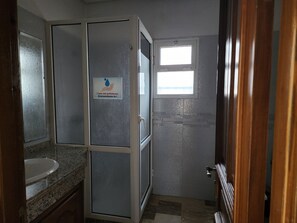 A bathroom with a shower enclosure, a sink, and a window.