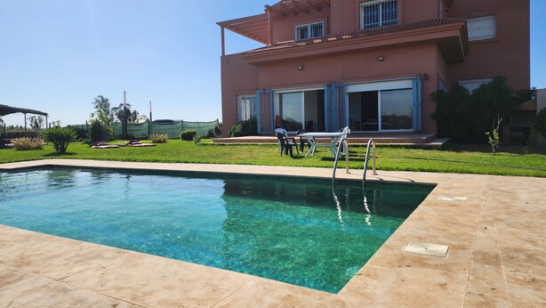 Una piscina con agua cristalina, un patio y una casa grande con techo de tejas.