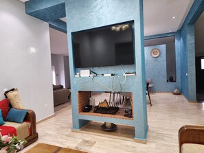 Ein Wohnzimmer mit an einer blauen Wand montiertem Fernseher, einer Couch, einem Couchtisch und einer dekorativen Vase.