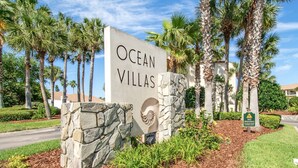 A sign for Ocean Villas with a stone base and palm trees in the background. - First Floor Condo, Two Pools, One Heated Pool, Easy Beach Access, Large Patio, $300 in Free Tickets! (St. Augustine Beach)