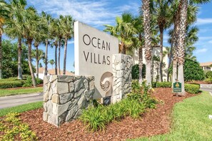Schild für Ocean Villas mit Steinunterbau und Palmen im Hintergrund.