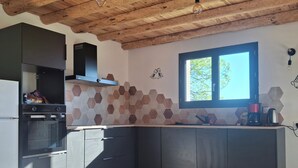 A modern kitchen with a built-in oven, dark cabinets, a hexagonal tile backsplash, and a window with a view of trees. - Quiet house in the mountains (Montselgues)
