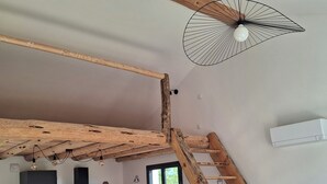 A loft-style room with exposed wooden beams, a kitchen area, and a wooden ladder leading to an upper level. - Quiet house in the mountains (Montselgues)