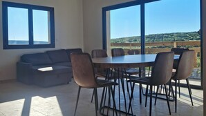 A dining area with a table and chairs, a sofa, and large windows with a view of a hilly landscape. - Quiet house in the mountains (Montselgues)
