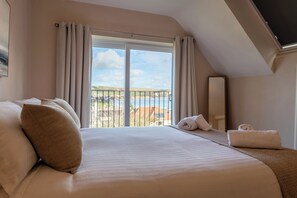 A hotel room with a large bed, a view of the sea, and a balcony with a railing. - Bay View | Swanage sea view, walk to beach, sleeps 9, dog friendly, hot tub (Swanage)