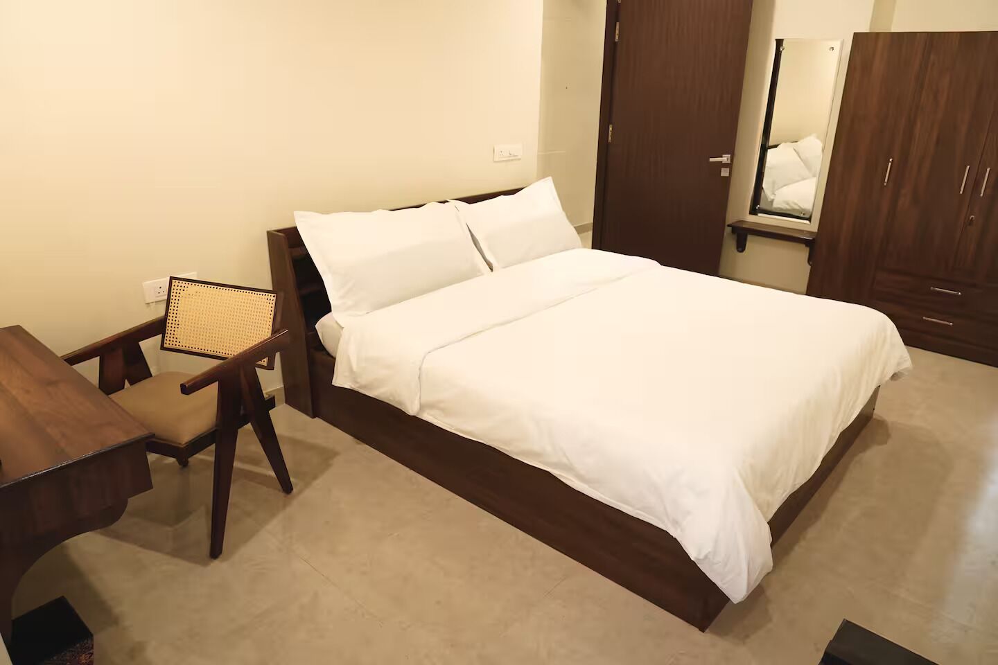 Un dormitorio ordenado con cama, una silla, un escritorio y un armario.