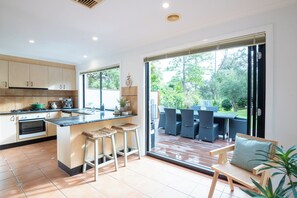 A modern kitchen with a large island, bar stools, and a dining area with a view of the garden. - Charles Retreat (Rye)
