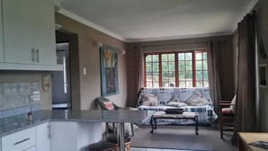 Eine Küche mit Marmorarbeitsplatte, ein Essbereich mit gemustertem Tischleinentuch und ein Fenster mit Vorhängen.
