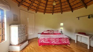 Ein Schlafzimmer mit Holzboden, einem Bett mit rotem und weißem Überwurf, einem Schminktischchen, einem Nachttisch und einem Fenster.