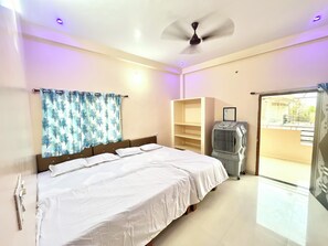 Een hotelkamer met een bed, een plafondventilator, een verwarming, een raam met uitzicht en een deur naar een balkon.