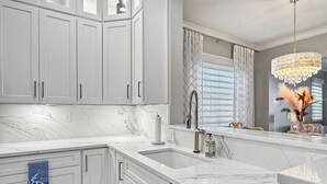 Una cocina moderna con armarios blancos, encimera de mármol, un lavamanos y una araña.