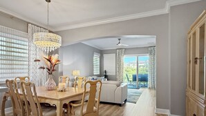 Comedor con mesa y sillas de madera, una araña y vista a un balcón con mobiliario exterior.