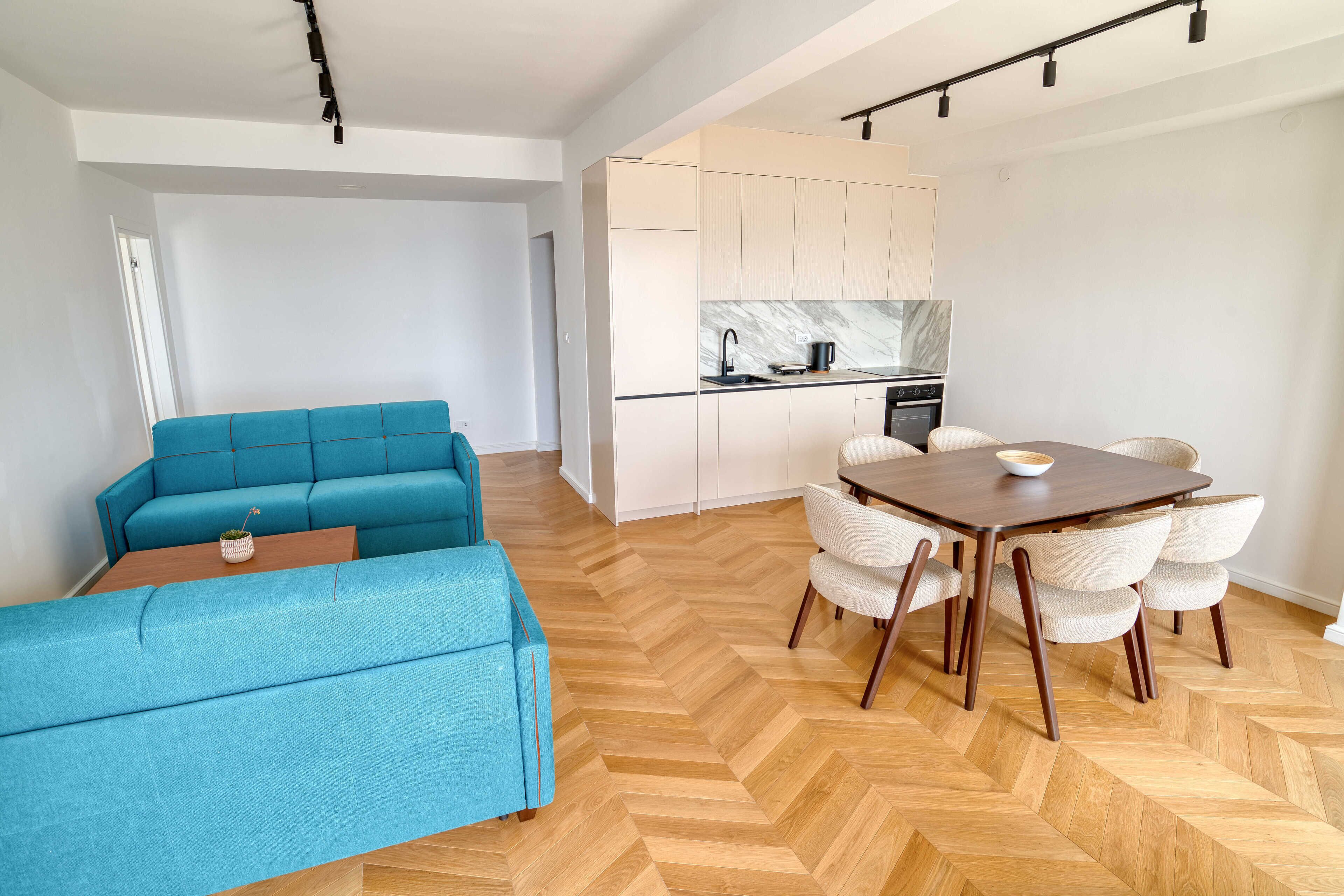 Ein modernes Wohnzimmer mit einem blauen Sofa, einem Holzespeisesaal mit Stühlen und einer Küchenzeile mit Schränken und einer Marmor-Spritzschutzwand.