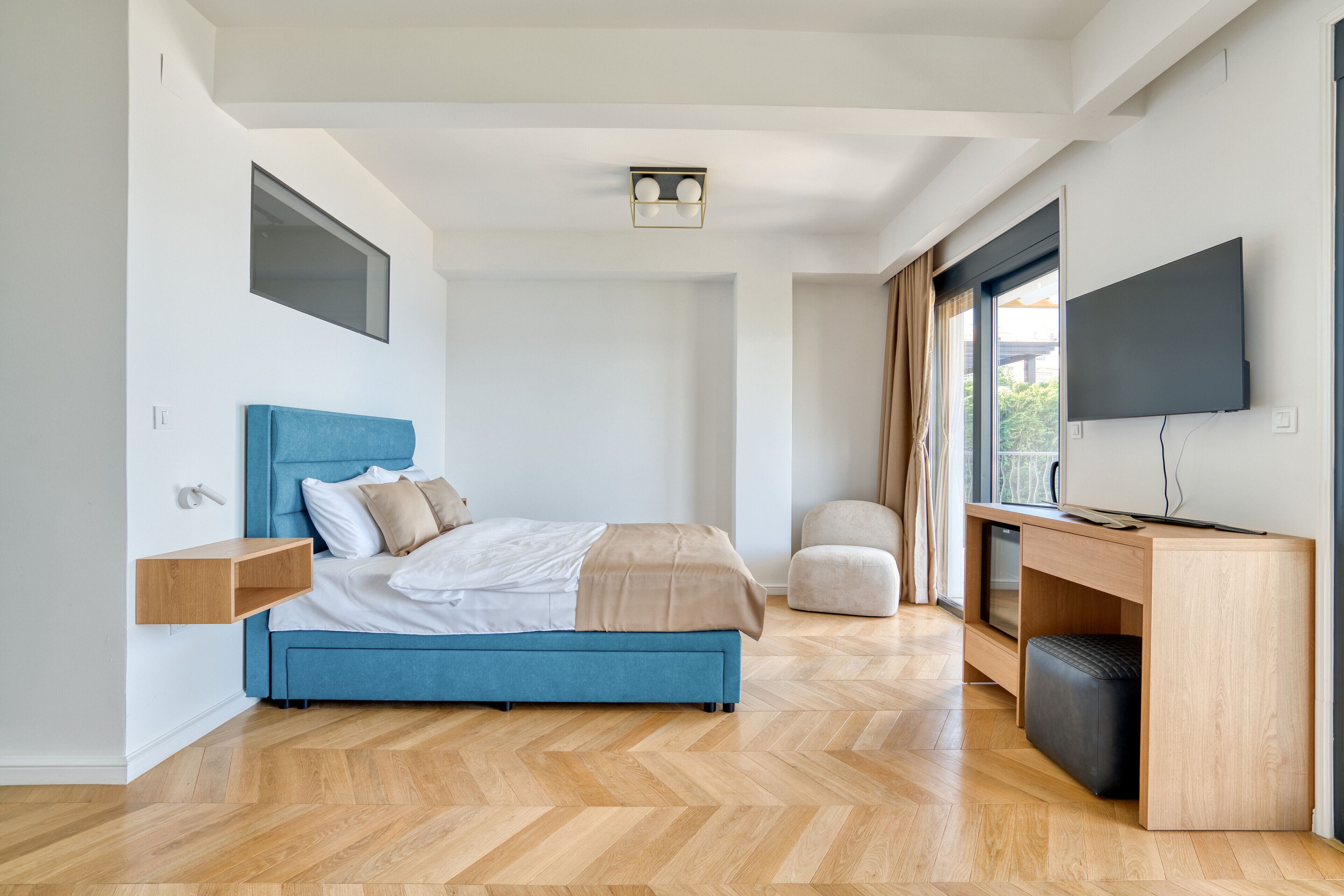 A modern bedroom with a bed, bedside tables, a desk, a TV, and a window.