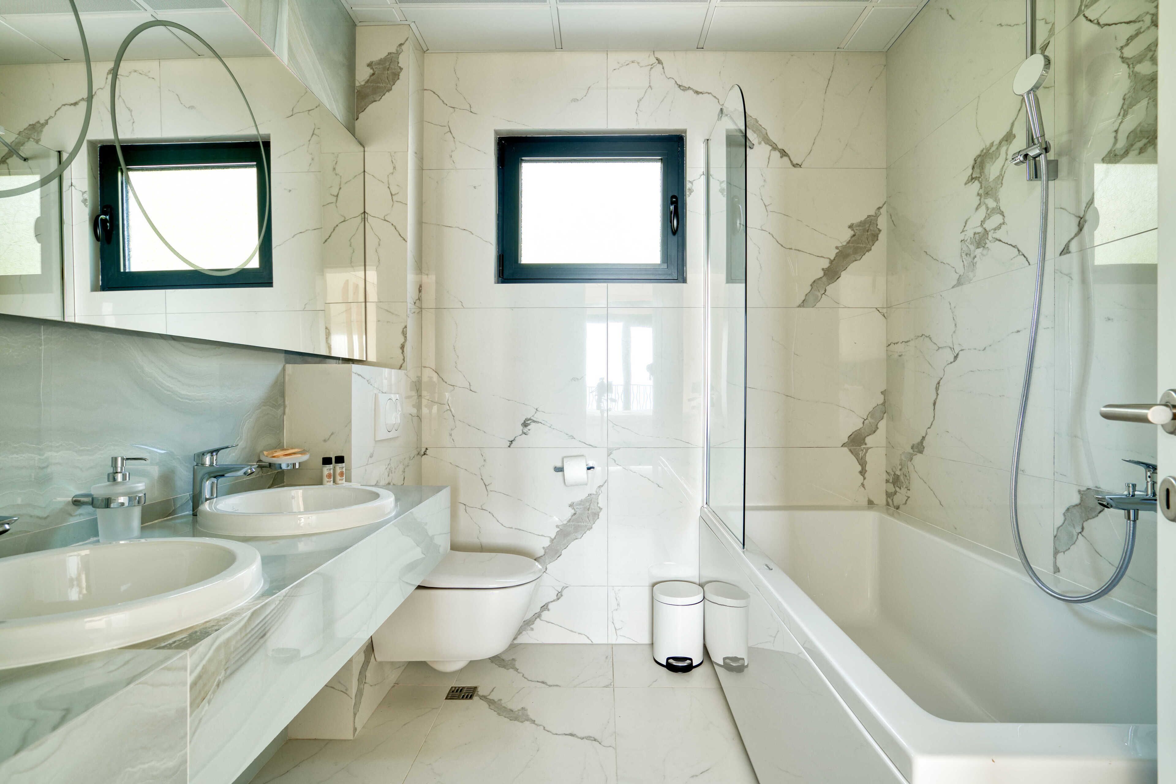 A modern bathroom with two sinks, a toilet, a shower, and a window.