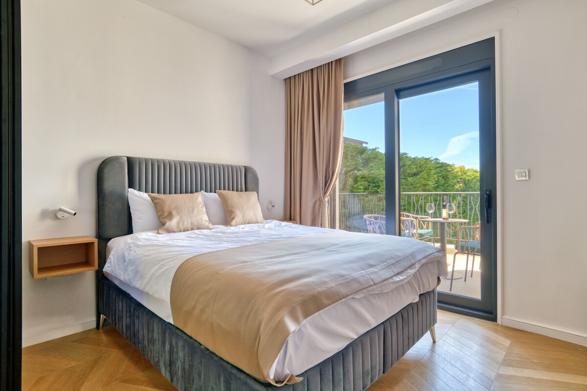 Quarto com cama, mesa de cabeceira, porta de correr para uma varanda e vista para o verde.