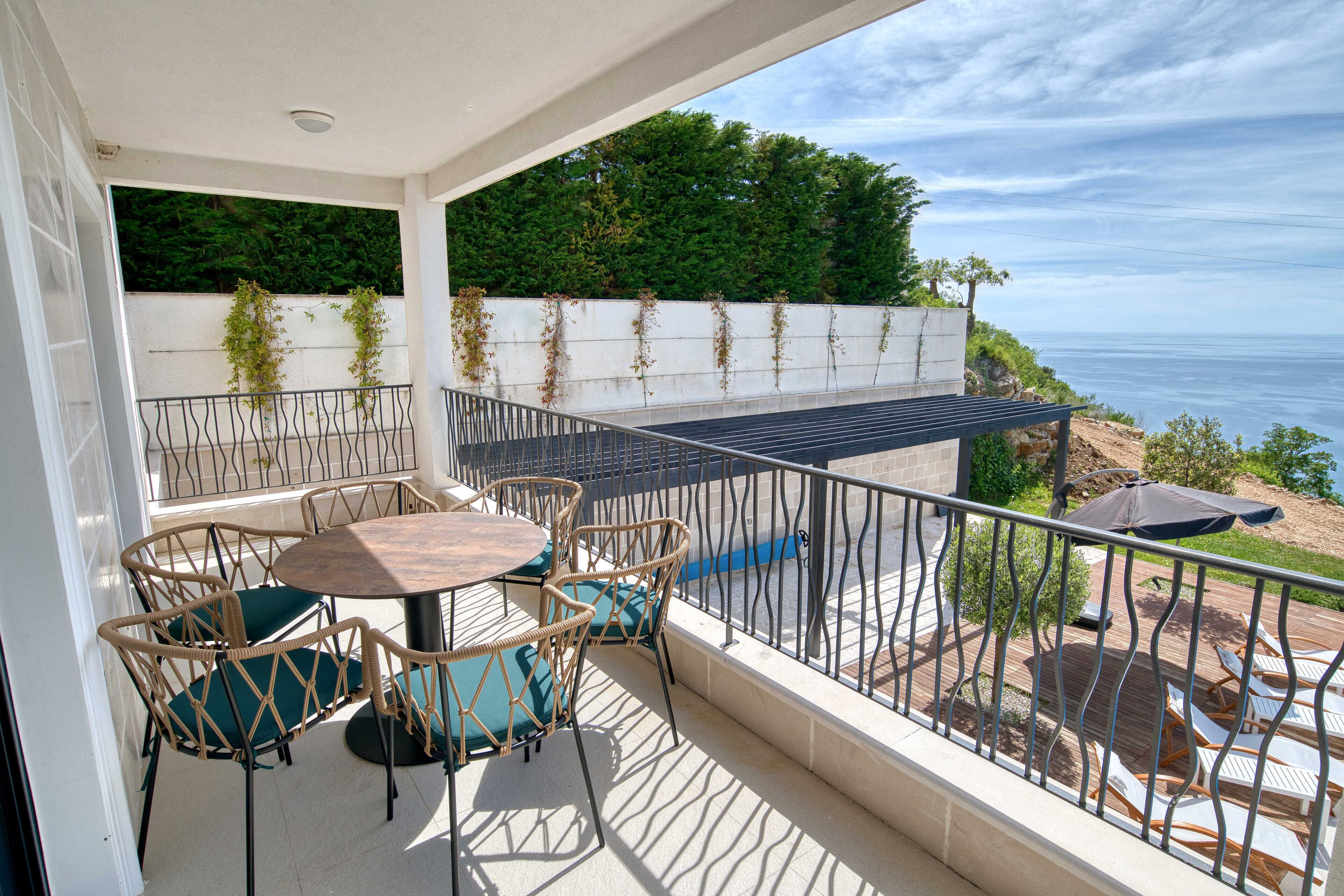 A balcony with a table and chairs, a view of the sea, and a railing.